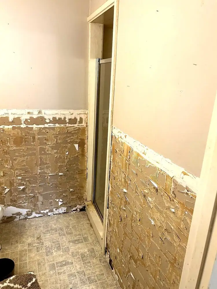 In-progress bathroom remodel showing a glass shower enclosure and partially removed wall tile