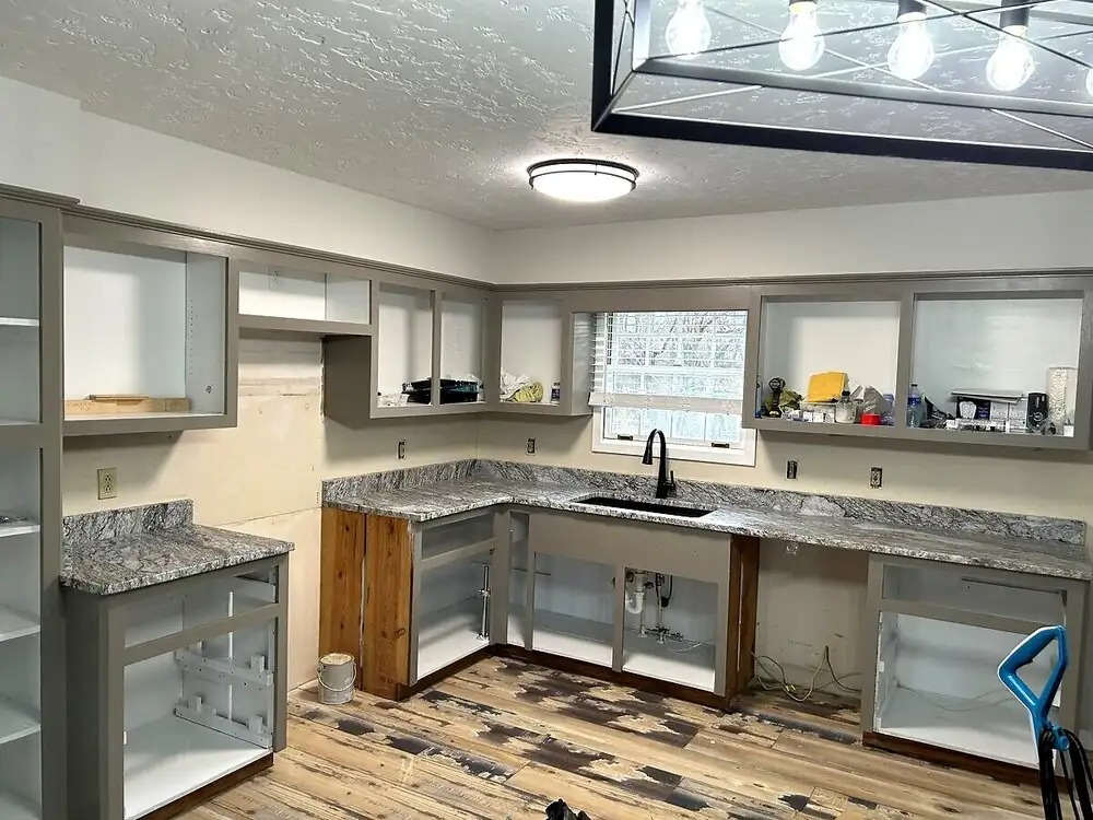In-progress kitchen remodel with gray cabinets, granite countertops, and a black sink under a window