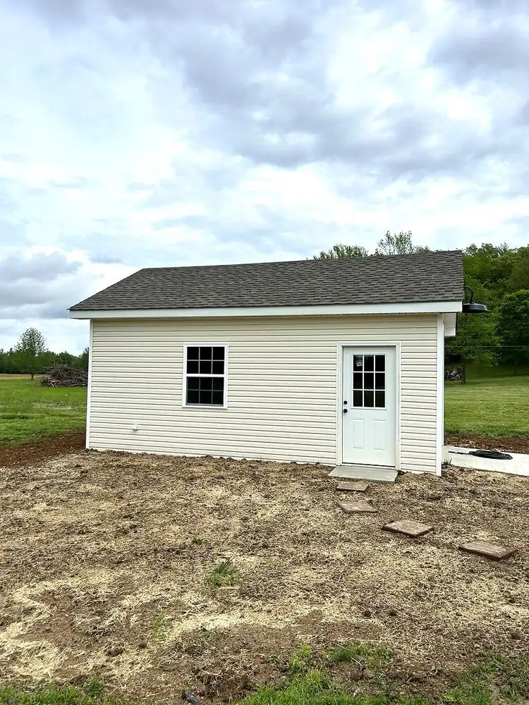 Beige vinyl-sided shed with white door and window in a rural Kentucky setting