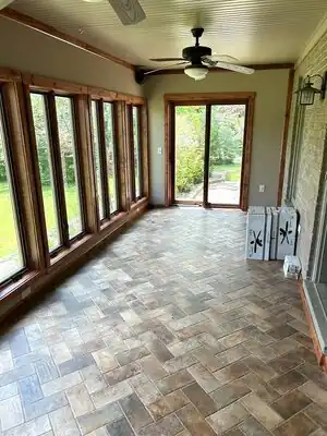 Interior of enclosed sunroom with wall of windows, sliding door, wood trim, ceiling fan, and tiled floor.