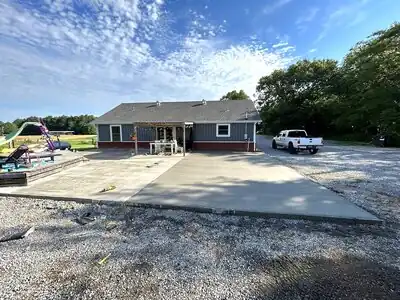 Single-story gray house with brick base, new concrete driveway and front porch, white pickup truck, and a playground in rural Murray, KY.