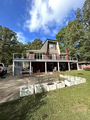 Two-story brick house with a large elevated deck under construction in Murray, KY; planters and tools in foreground.