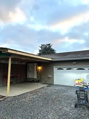 Front view of a house with a new covered porch under construction, wooden posts, siding, and a garage.