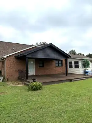 {
  "description": "A single-story brick home features a newly completed dark-roofed covered porch extension with a wooden de