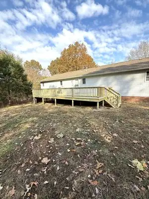 New wooden back deck attached to white house in Kentucky; stairs lead to yard with autumn leaves.